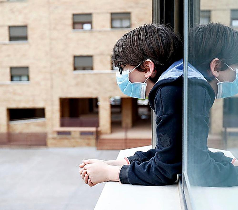 Un niño con una mascarilla se asoma a la ventana de su casa cuando queda tan solo una semana para que niños y preadolescentes puedan salir a la calle durante el confinamiento por el coronavirus, en Valdemoro/Madrid (España) a 20 de abril de 2020.  / ÓSCAR J.BARROSO   EUROPA PRESS