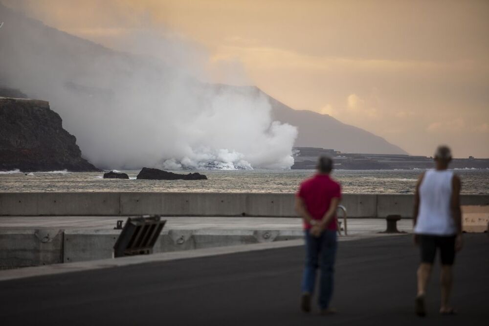 Dos personas observan la columna de humo y la lava del volcán de Cumbre Vieja a su llegada al Océano Atlántico
