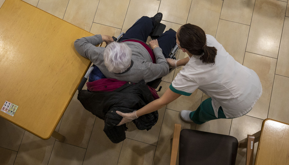 La trabajadora de un centro de atención a mayores atiende a una persona de avanzada edad, en silla de ruedas.